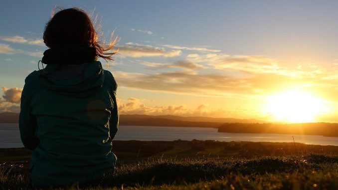 Frau sitzt in der Abendsonne am See