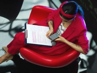 frau mit unterlagen und handy im roten stuhl