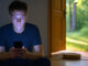 junger Mann mit Handy vor geöffneter Gartentür